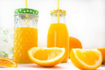 Healthy orange juice in a glass jar and a bottle stands on a white background. In the foreground are two slices of juicy orange. Healthy nutrition, vitamins, detox diet. Close-up, selective focus.