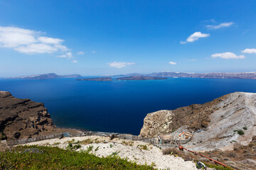 Fototapeta na wymiar Santorini, Caldera, view from the rocky coastline of the Caldera and two volcanic islands .In the background Oia. Down on the hillside a new house. Beautiful clear blue sky.