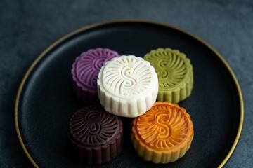 Colorful moon cakes are placed on black plates. Chinese traditional food mid autumn moon cake