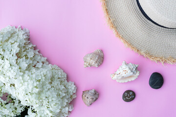 Flat lay on a pastel pink background. Hydrangea, shells and straw hat on a pink background. Vacation concept.
