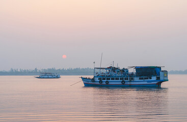 Bright Indian tourist boats in a lagoon on a background of morning sky and red rising sun.