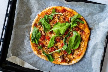 Homemade Pizza with Parmesan Cheese Slice, Rucola, Arugula or Rocket Leaves on Baking Tray with Sheet Paper.