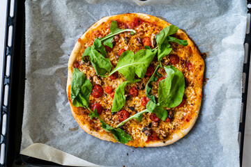 Homemade Pizza with Parmesan Cheese Slice, Rucola, Arugula or Rocket Leaves on Baking Tray with Sheet Paper.