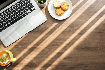 Wood office desk table with laptop computer, a dish of almond cookies and cup of latte coffee with...