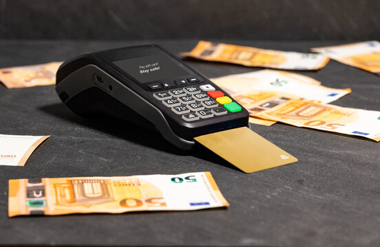 Paying with a gold card at the POS and around it some fifty euros banknote on black background. Stay safe! No cash!