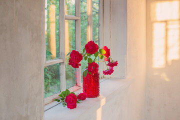 Fototapeta na wymiar red roses in red glass vase on windowsill