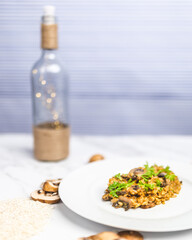 Mushroom risotto with Parmesan cheese and white Wine in a white serving plate on a white marble table with risotto Rice and raw mushroom on the side. Free space for your text/decoration.