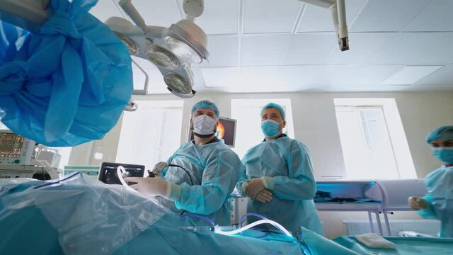 Operation for crushing stones. Medical workers in blue uniform and masks conduct a surgery in modern operating room in clinic.