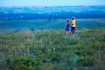 Naklejka na ściany i meble Two children in the summer stand in a field on a hill and look into the distance. Future vision concept. Walks in the open air. Family, little sisters walk and play together