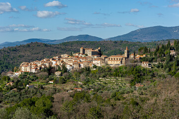 Fototapeta na wymiar Provencal village in the hinterland. Perched on a hill, the village has a church with a bell tower with a glazed tile roof. It is dominated by a castle with a round tower. Some white clouds in the blu