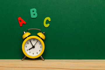 Back to school concept, with colorful wooden letters and yellow alarm clock on green wooden background