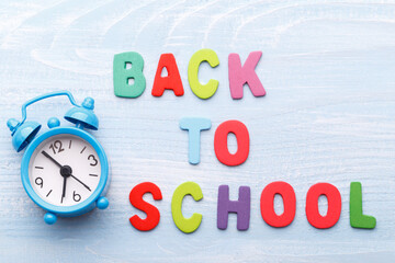 Back to school concept, with colorful wooden letters and alarm clock on blue wooden background