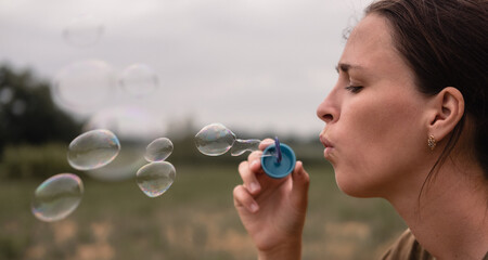 The girl blows soap bubbles. A young woman sits in nature and blows soap balls. Face in profile.