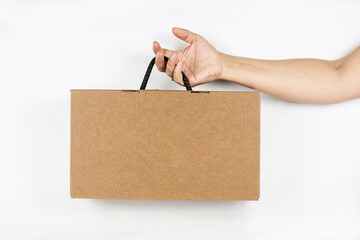 Female hand holding a cardboard box made of corrugated cardboard on a light background. The woman...