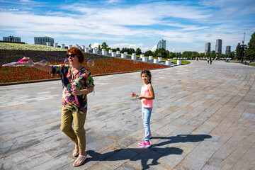 Fototapeta premium grandmother and beautiful girl who poses with soap bubbles in the park