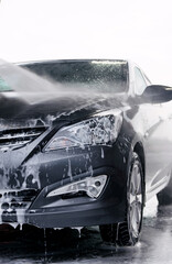 Detergent is washed off the front of a gray car with water