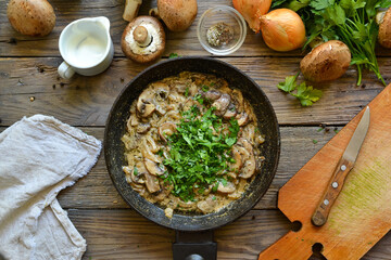Royal champignons in sour cream sauce. Recipe. Step by step cooking mushrooms with onions. Wood background. Top view. Mushrooms with onions and sauce in a pan and parsley.