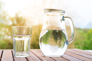jug with water and a glass on a wooden table on the nature in the garden