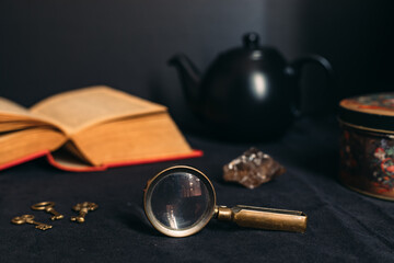 Collection of mysterious items: old book, magnifying glass, little keys, black tea pot, stone and...