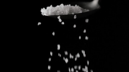 Coarse sea salt crystal falling from spoon on black background in slow motion