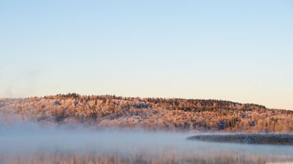 Dancing fairies, mist, lake, calm water, sunlit trees. Beautiful morning at sunrise, dawn in early winter.  Blue sky background with place for text, copy space.