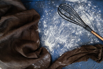 Kitchenware for cooking. Whisk and flour on a dark blue background. Linen fabric for decoration.