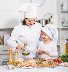 Woman with her daughter are cooking salad in uniform in the kitchen at home.