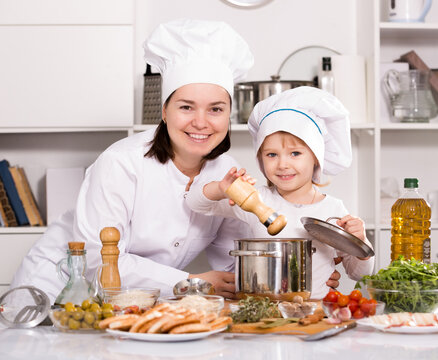 Girl and her mother are cooking soup together and adding spices in the kitchen at home.