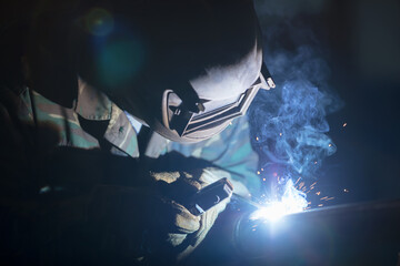 Welder at work. Man in a protective mask. The welder makes seams on the metal. Sparks and smoke...