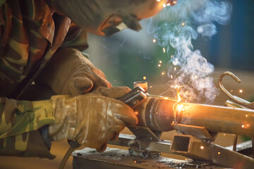Welder at work. Man in a protective mask. The welder makes seams on the metal. Sparks and smoke...