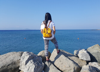 A teenage girl is looking dreamily at the horizon over the bright blue sea. Photographed on the...