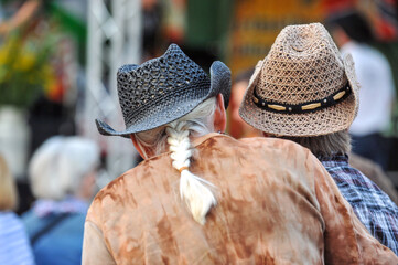 Ein Ã¤lteres Paar in Western und Country Outfit und Cowboyhüten auf einer Open-Air-Veranstaltung vor der Bühne - selektiver Fokus, viel Copy Space
