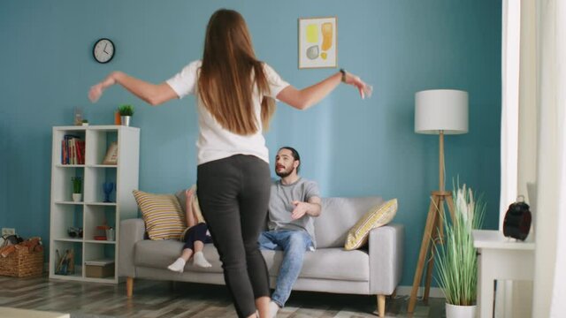 Young pretty woman is playing pantomime with her family, showing butterfly, child and father are guessing, all have fun together, happy moment of life, Slow motion.