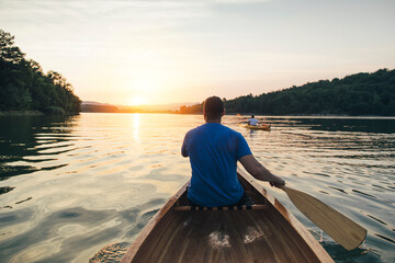 Rear view of men paddling canoe and kayak at sunset lake