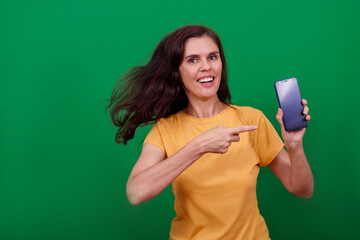 Young attractive woman is pointing on blank screen of phone in her hand and looks into a camera