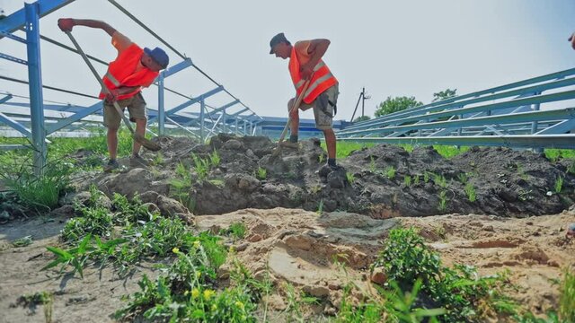 Construction industry. Workers in protective uniform build solar farm on the ground. Engineers digging during building works. Slow motion.
