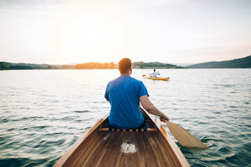 Rear view of man paddling canoe while friend kayaking in background