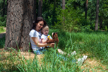 Mother with daughter sitting in the forest and resting with toys. Small girl and her mom outdoors have fun © galika