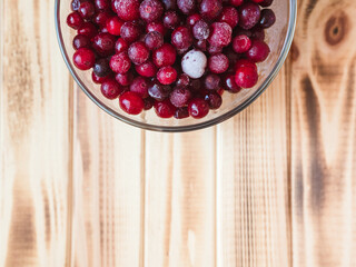 frozen wild cranberries in a glass cup on a wooden table, flat lay, copy space