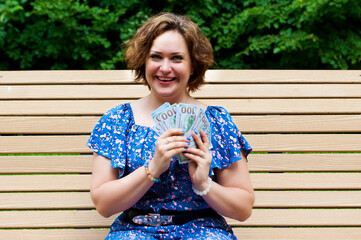 Blonde woman holding in arms money and happy smiling in the park. Female win cash