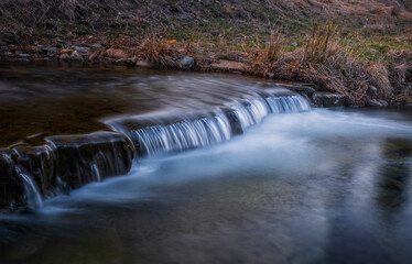 Obraz premium Water threshold on river Zalotomyatyi in carpatian mountains and green forest. National park Skolivski Beskidy. April 2020. Long exposure shot.