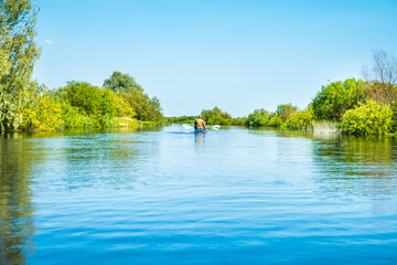 People on kayak trip on blue river landscape and green forest with trees blue water clouds sky