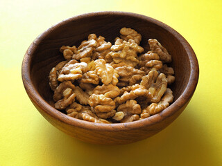 Walnuts in a wooden bowl on a yellow background