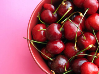 Sweet cherry in a red bowl on a pink background.