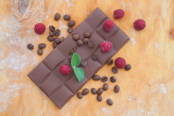 chocolate bar with coffee beans and raspberry on a wooden background view from above
