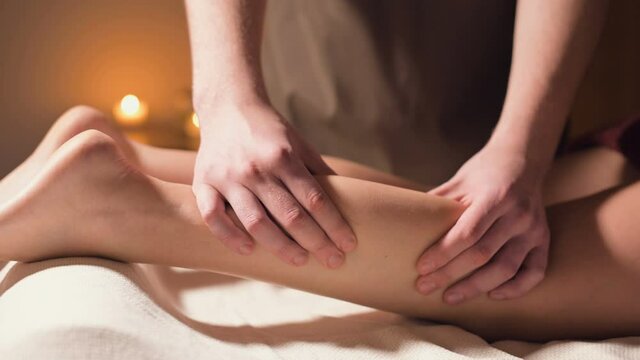 Close-up of the hand massage of the calf muscle. A professional massage therapist massages a woman's leg in an office with a beautiful light