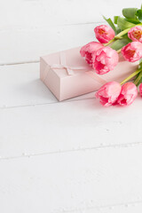 a bunch of tulips and a gift box on white wood table. copy space.
