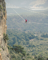 Obraz premium A man is walking along a stretched sling. Highline in the mountains. Man catches balance. Performance of a tightrope walker in nature. Highliner on the background of valley.