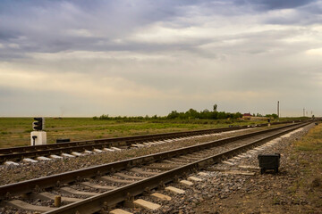 Railway at sunset. Railroad station. Railroad crossing. Railway signs at the crossroads. Sky with rain clouds at sunset. Clouds in the sky. Rails, sleepers, stones. Perspective. Horizon