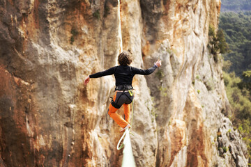 A man is walking along a stretched sling. Highline in the mountains. Man catches balance....